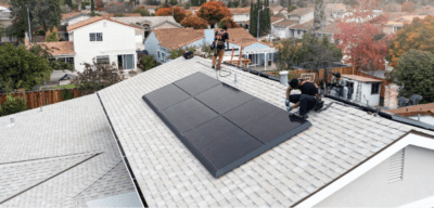 Two men are on top of a roof installing solar panels.