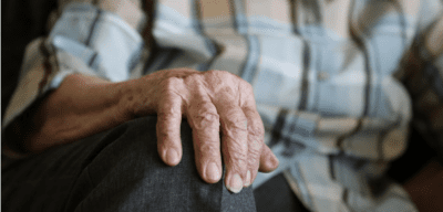 image shows the hands of an elderly woman putting her hand on her knee