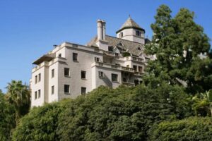 Image of a hotel in Los Angeles, Chateau Marmont, on a hill with green shrubs all around.