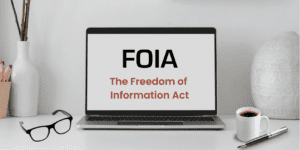 Freedom of Information Act written on a laptop, with glasses, coffee, a vase, a pencil holder and a pen