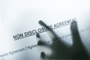 A hand shows up behind a paper with the typed words: "non disclosure agreement."