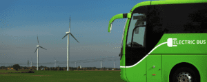 A green electric bus with with windmills in the background.
