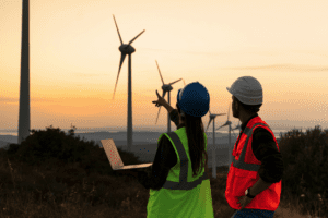 A woman and a man in a wind farm looking at the equipment. Both are wearing safety vests.