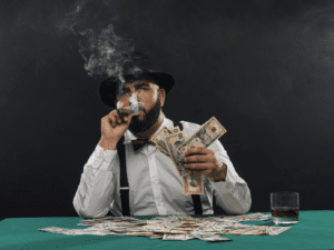 Man wearing a top hat and smoking a cigar has a pile of cash in front of him. Evokes gambling.