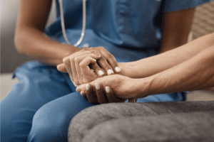 Image of a woman in blue scrubs holding the hand of someone else, in a caring way.