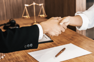 Two people shaking hands. One person is wearing a suit. There is a Scales of Justice in the background.