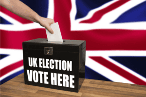 Image of a voting box that says "UK Election: Vote Here." The UK flag is in the background.